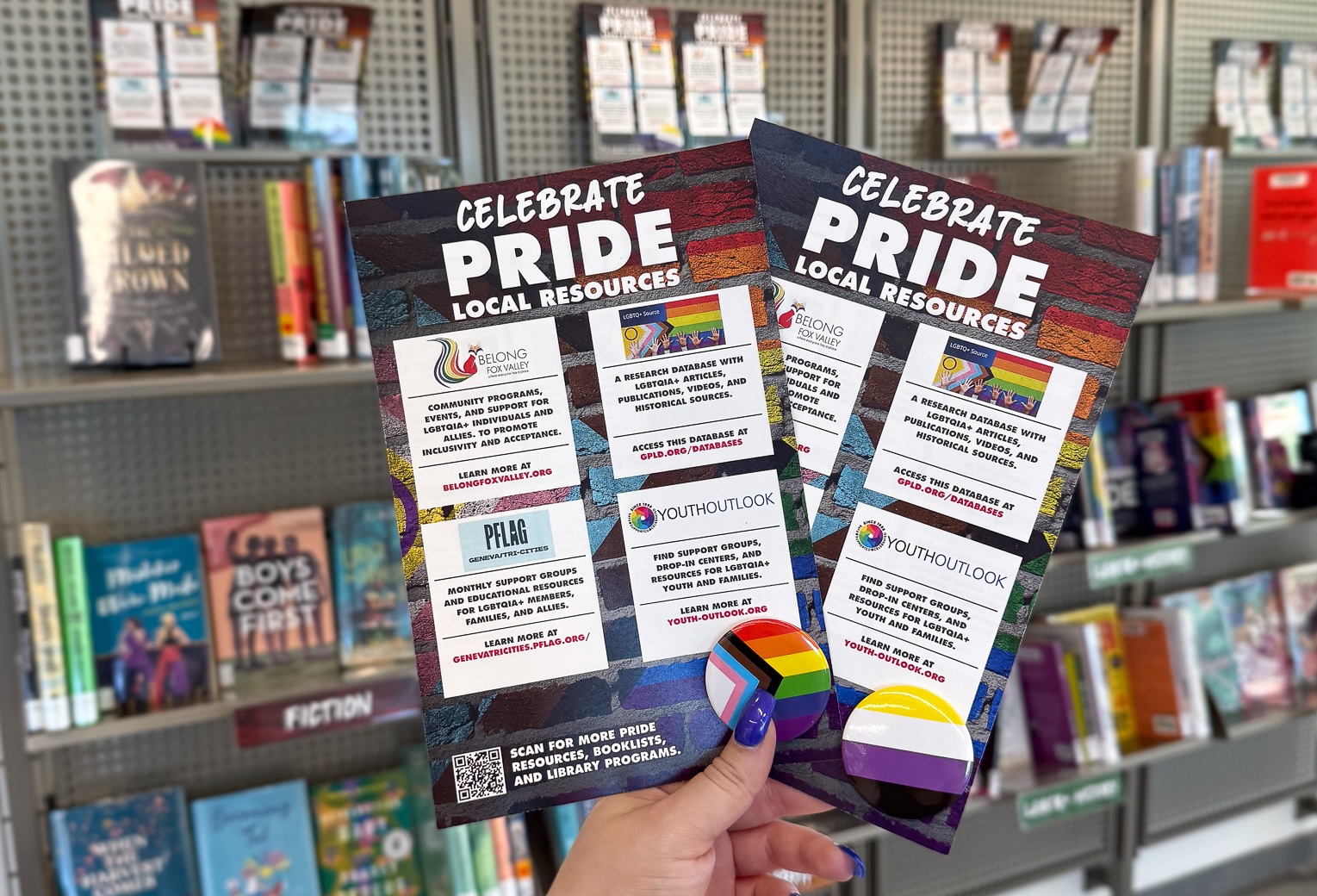 A hand holding local pride resources with pride buttons.
