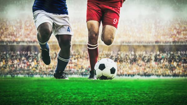 Two soccer players kicking a ball in a stadium.
