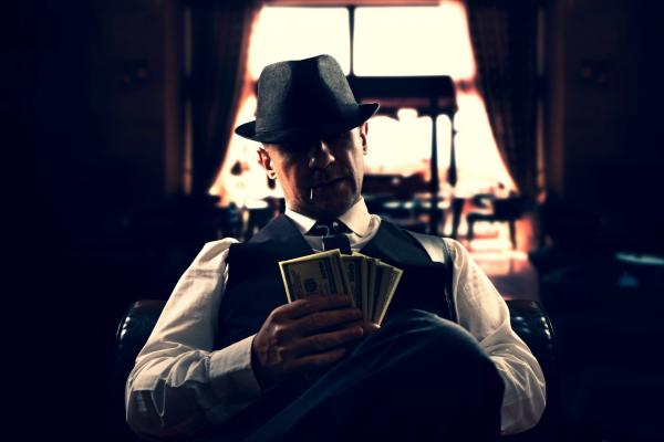 A man in gangster attire holding a fanned stack of money.