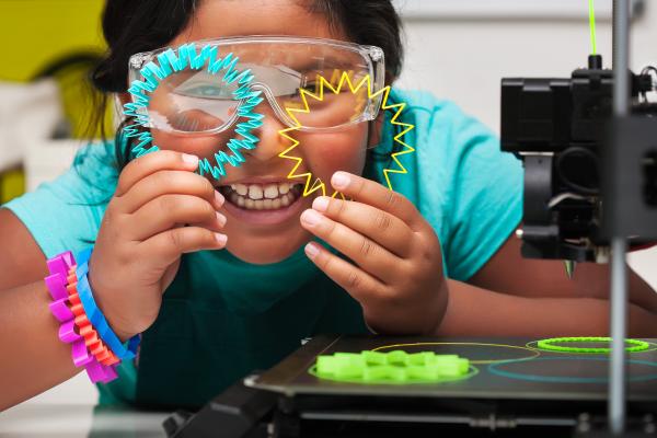 STEM student smiles and shows off the colorful 3d printed shapes, plastic parts on the print bed with skirt for plate adhesion.