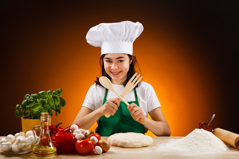 Teen in an apron and chef hat smiling with fresh ingredients.