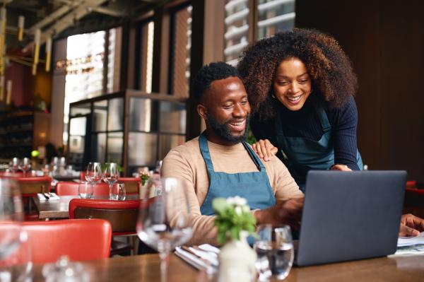 Two smiling young adults looking at a laptop screen.