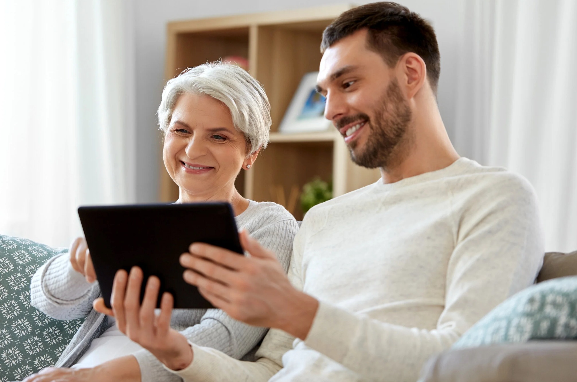 A senior and a young man smiling with a tablet.