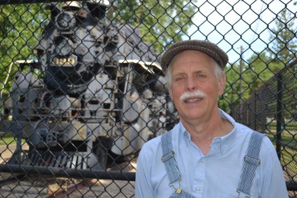 Mike Matejka in a train conductor's uniform in front of a steam train.