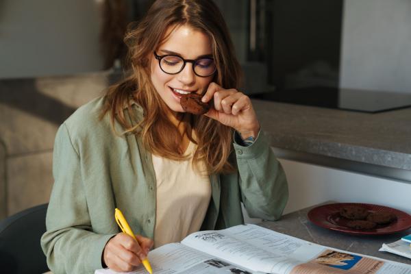 Girl eating a brownie while taking notes.