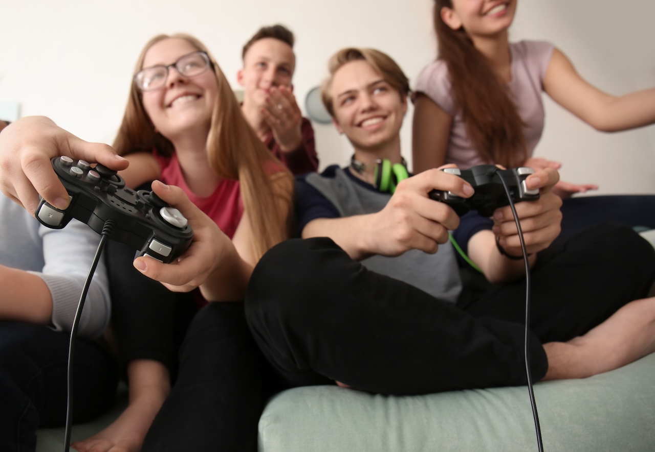 Teens smiling with wired game controllers.